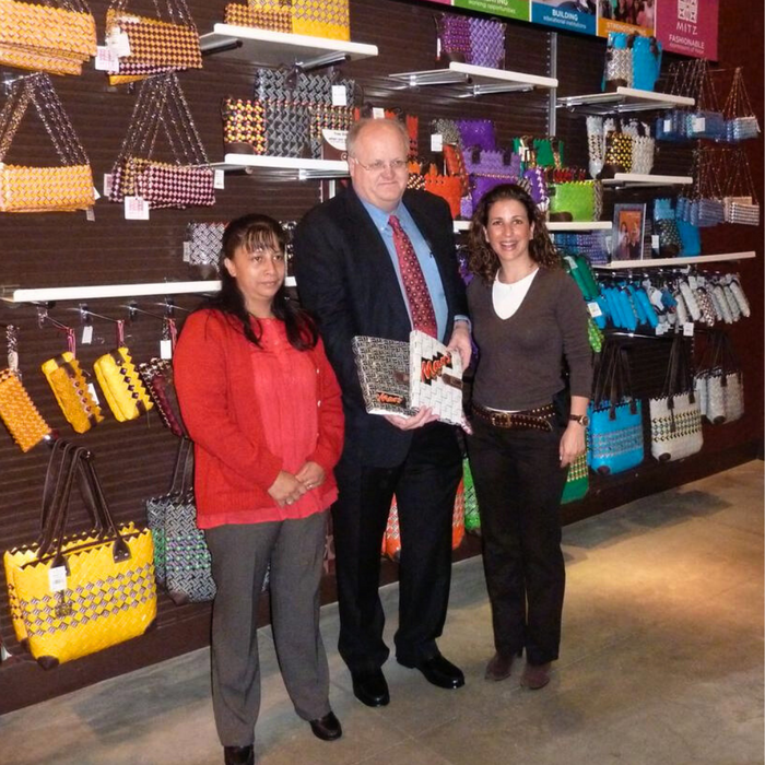 Exhibidor con bolsos y accesorios MITZ en un punto de venta, con tres personas presentando una pieza